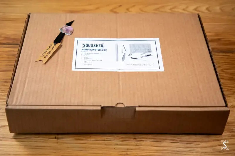 Cardboard box labeled Squished containing bookbinding tools kit for crafting enthusiasts