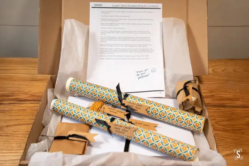 Diploma rolled in decorative holders inside a box of Coptic stitch bookbinding materials