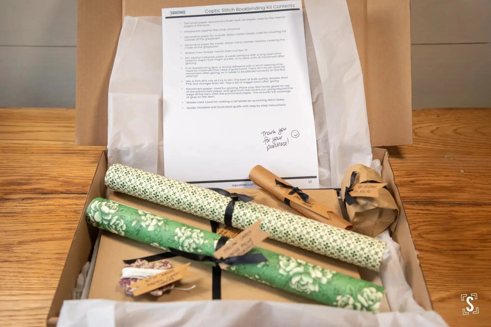 Open cardboard box containing wrapped gifts, a document, and wooden clothespins.