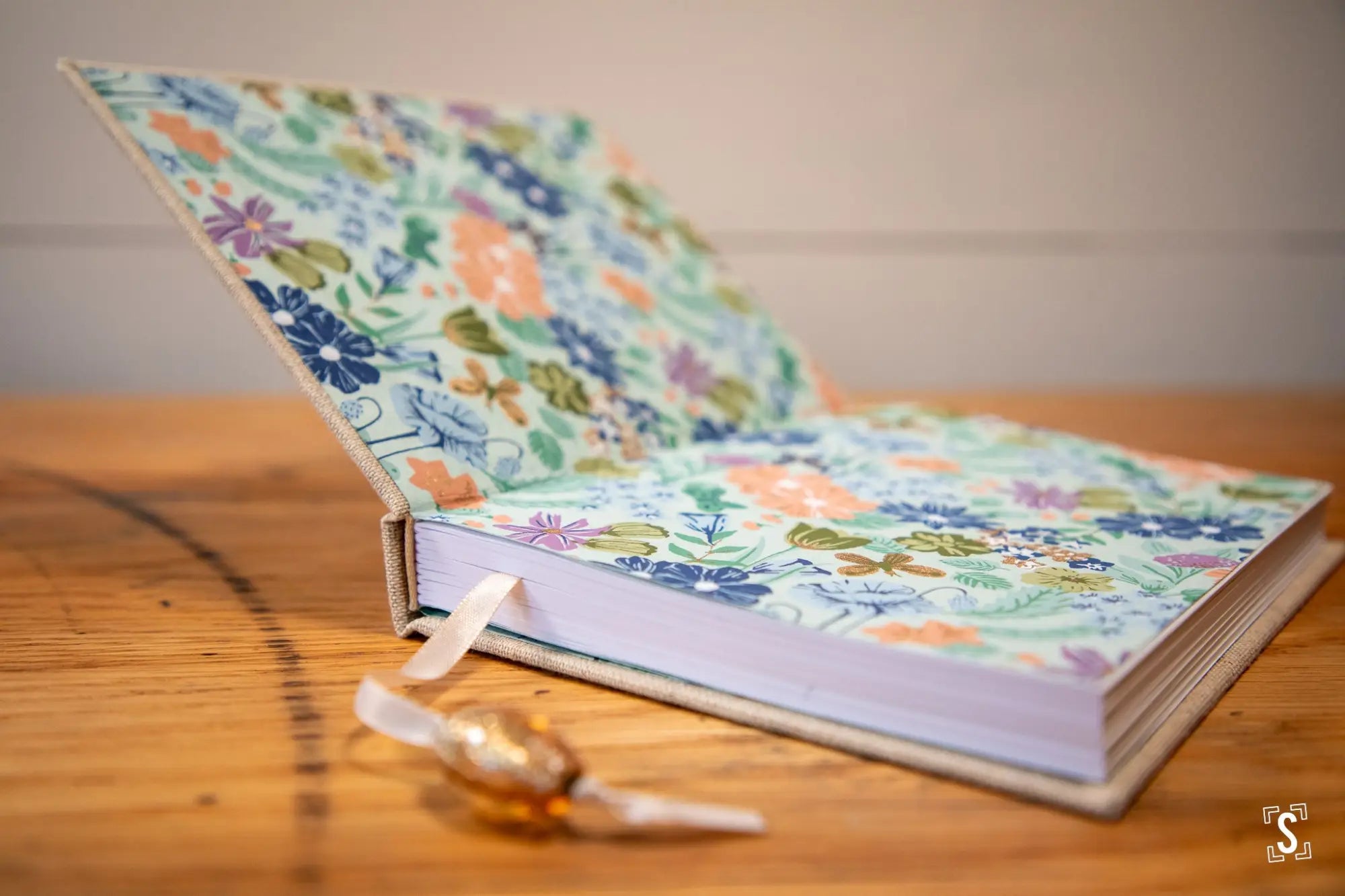 Floral-patterned hardcover book with a ribbon bookmark lying open on a surface.