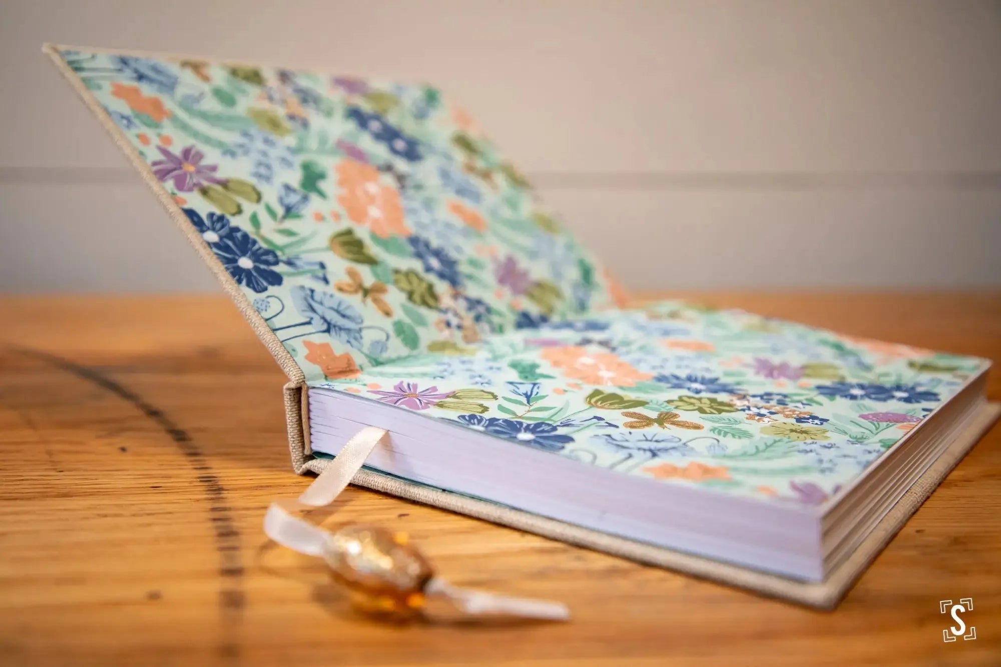 Floral-patterned hardcover book with a ribbon bookmark lying open on a surface.