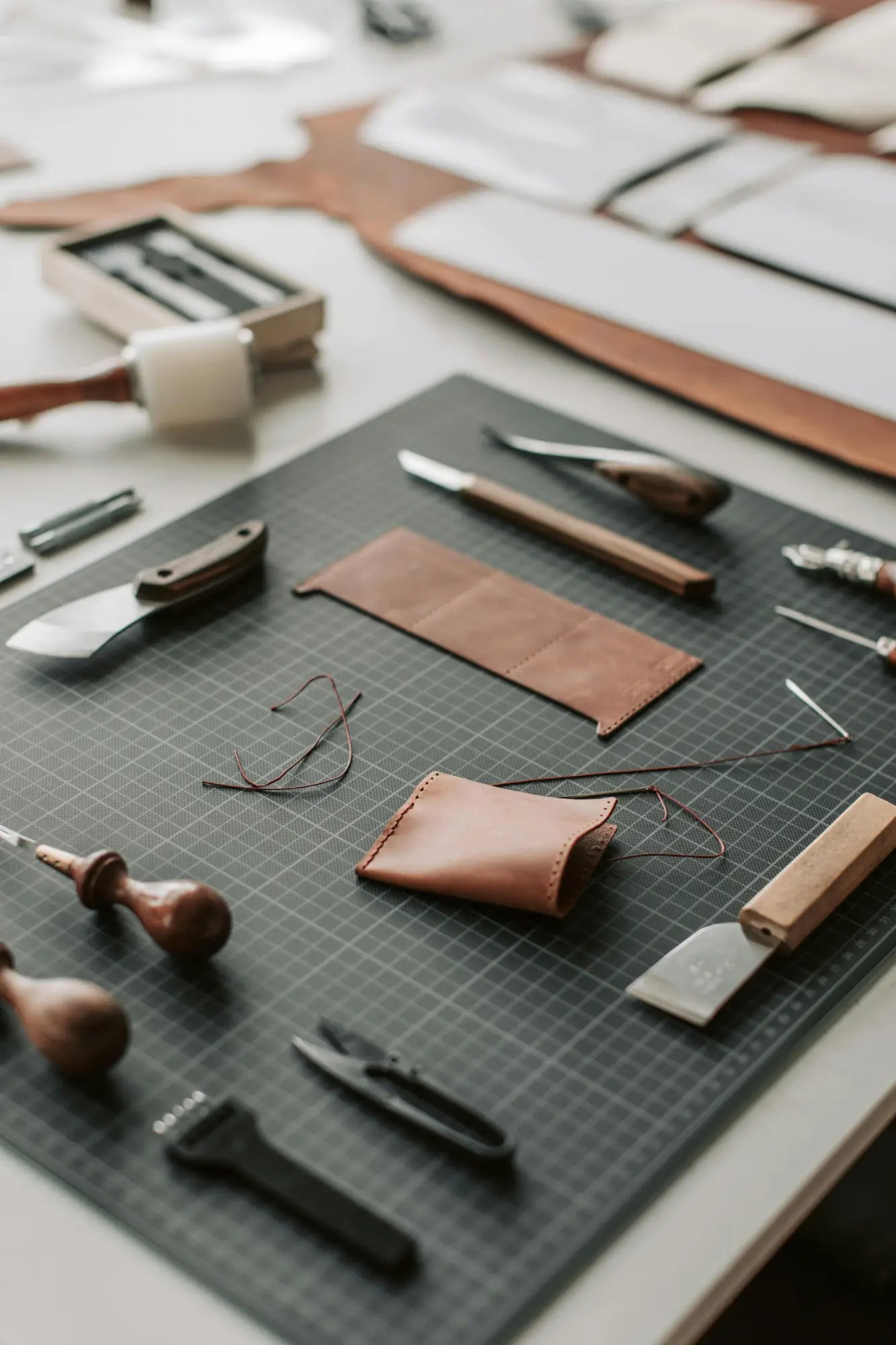 Collection of leatherworking tools and materials laid out on a cutting mat.