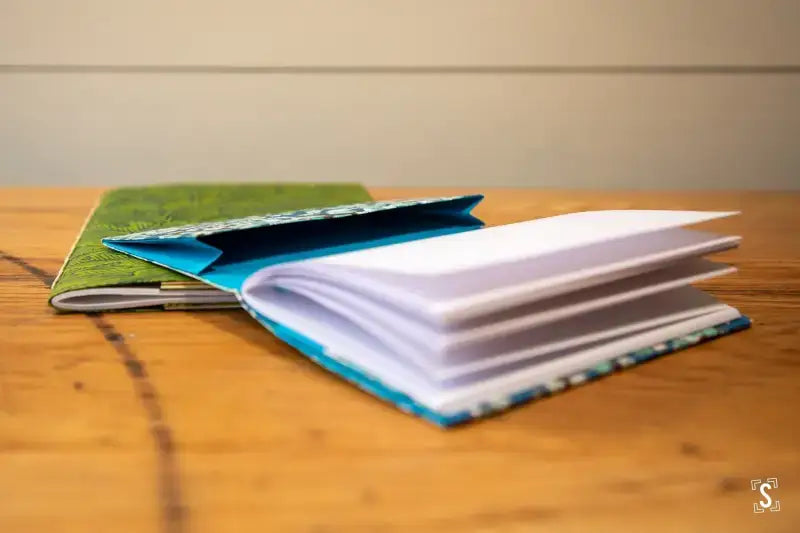 Colorful journals stacked on wood for Bookbinding Workshop featuring chain stitch technique