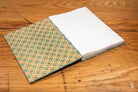 Patterned fabric notebook showcasing Coptic stitch design and a white page visible