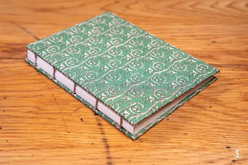 Handmade book with green patterned cover showcasing Coptic stitch binding at workshop