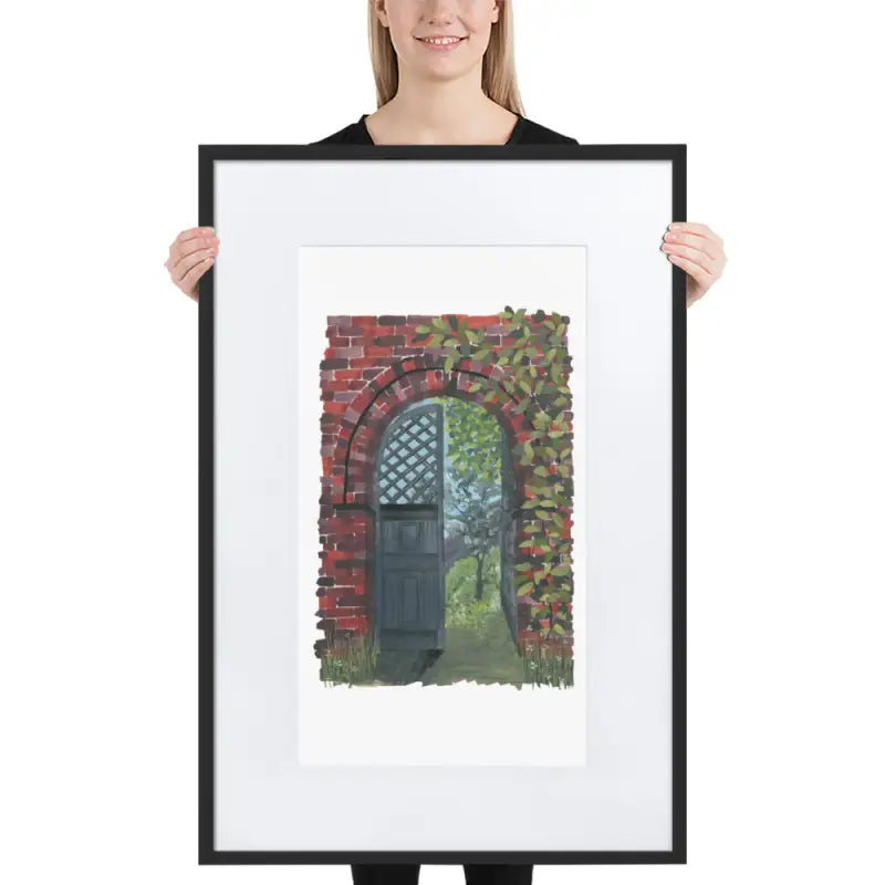 Woman holding a framed poster of a brick wall with a door in vibrant colours