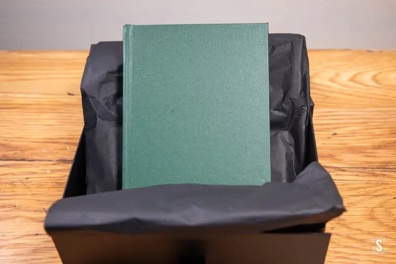 Green hardcover book in a black container, hand designed with Lokta endpapers and art prints