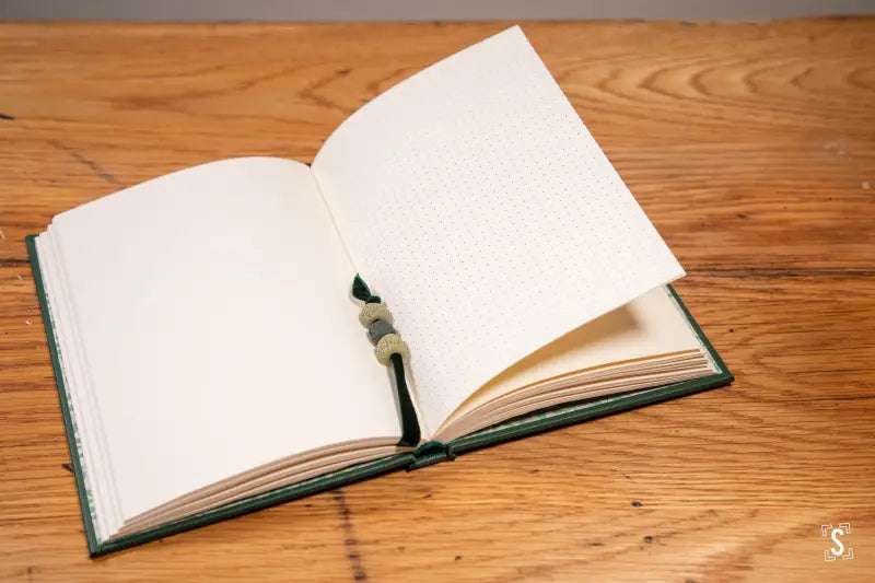 Open book on wooden surface showcasing hand designed buckram cover and blank pages