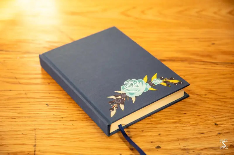 Navy blue book with mint green rose and gold leaf design, featuring Italian Carta Varese endpapers