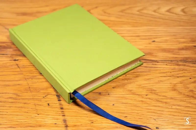 Lime green hardcover book with blue bookmark showcasing Italian Carta Varese endpapers