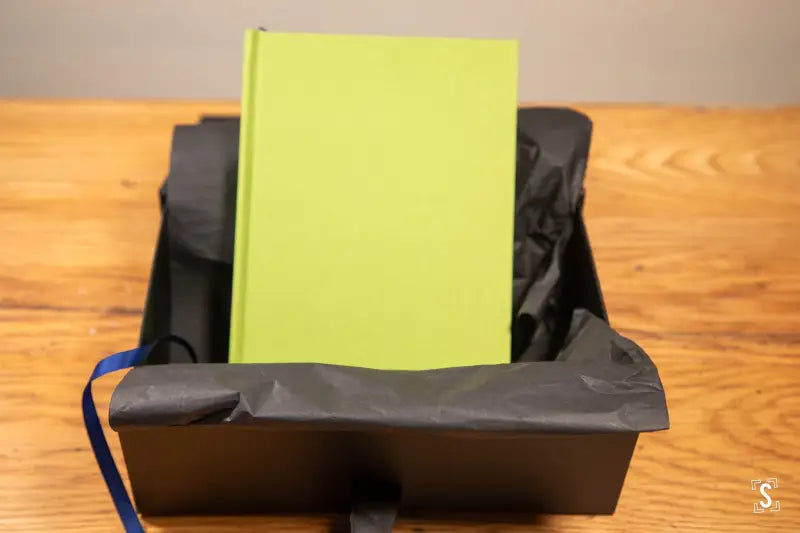 Bright yellow-green hardcover book in black container showcasing hand designed art prints