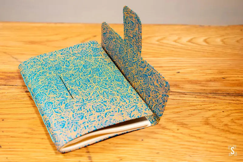 Decorative handmade book with turquoise and gold cover featuring tab closure and chain stitch