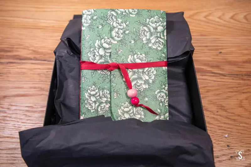 Black backpack with green floral prints and red ribbon atop a handmade book design