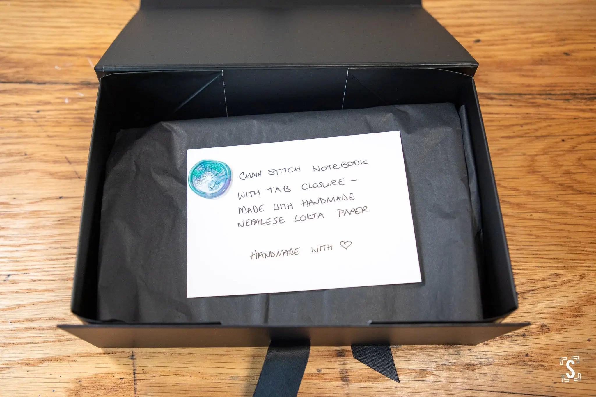 Black gift box holding a handcrafted art piece with a handwritten note on top