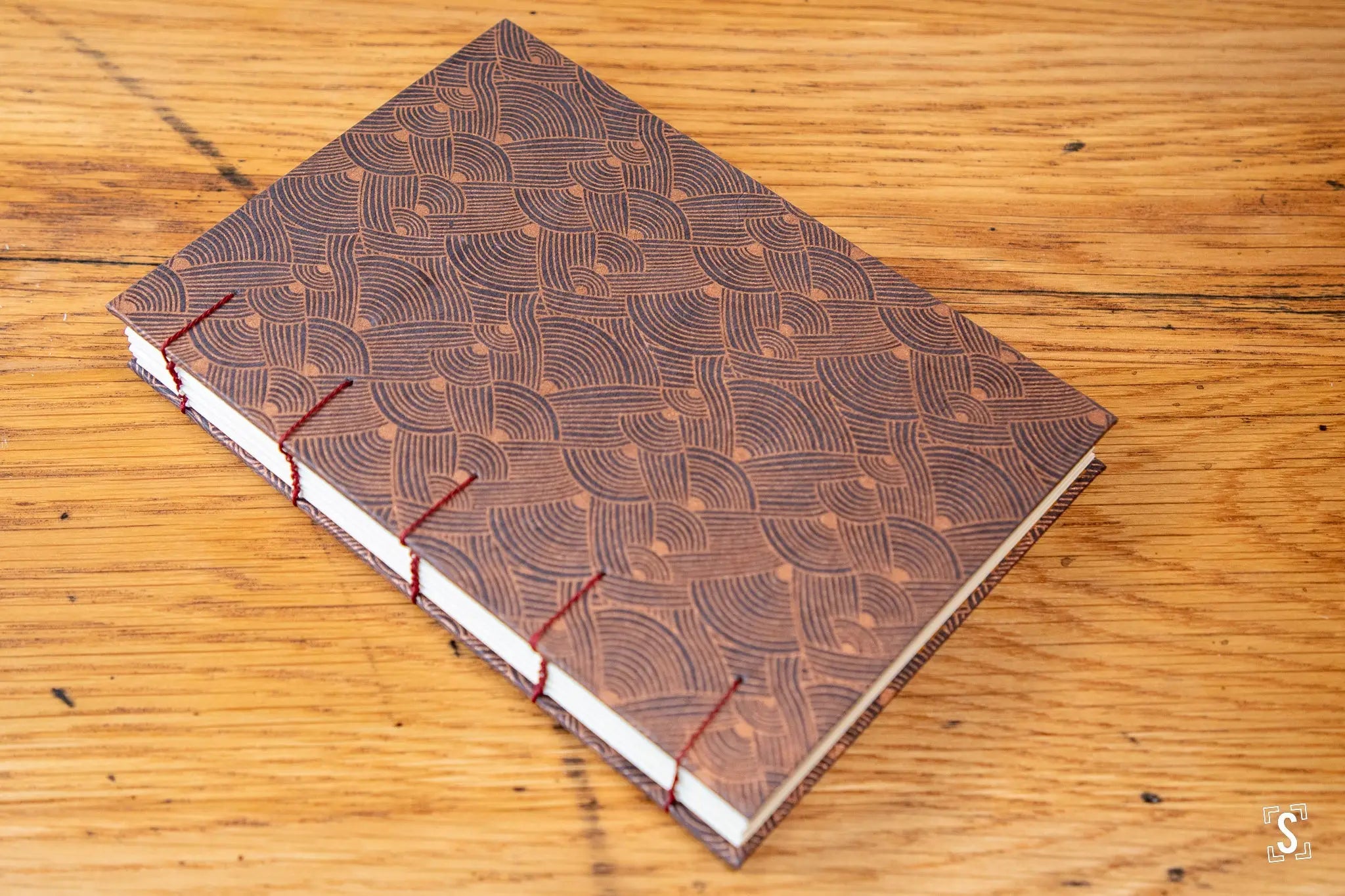 Hand designed handmade notebook featuring a brown patterned cover and red stitching