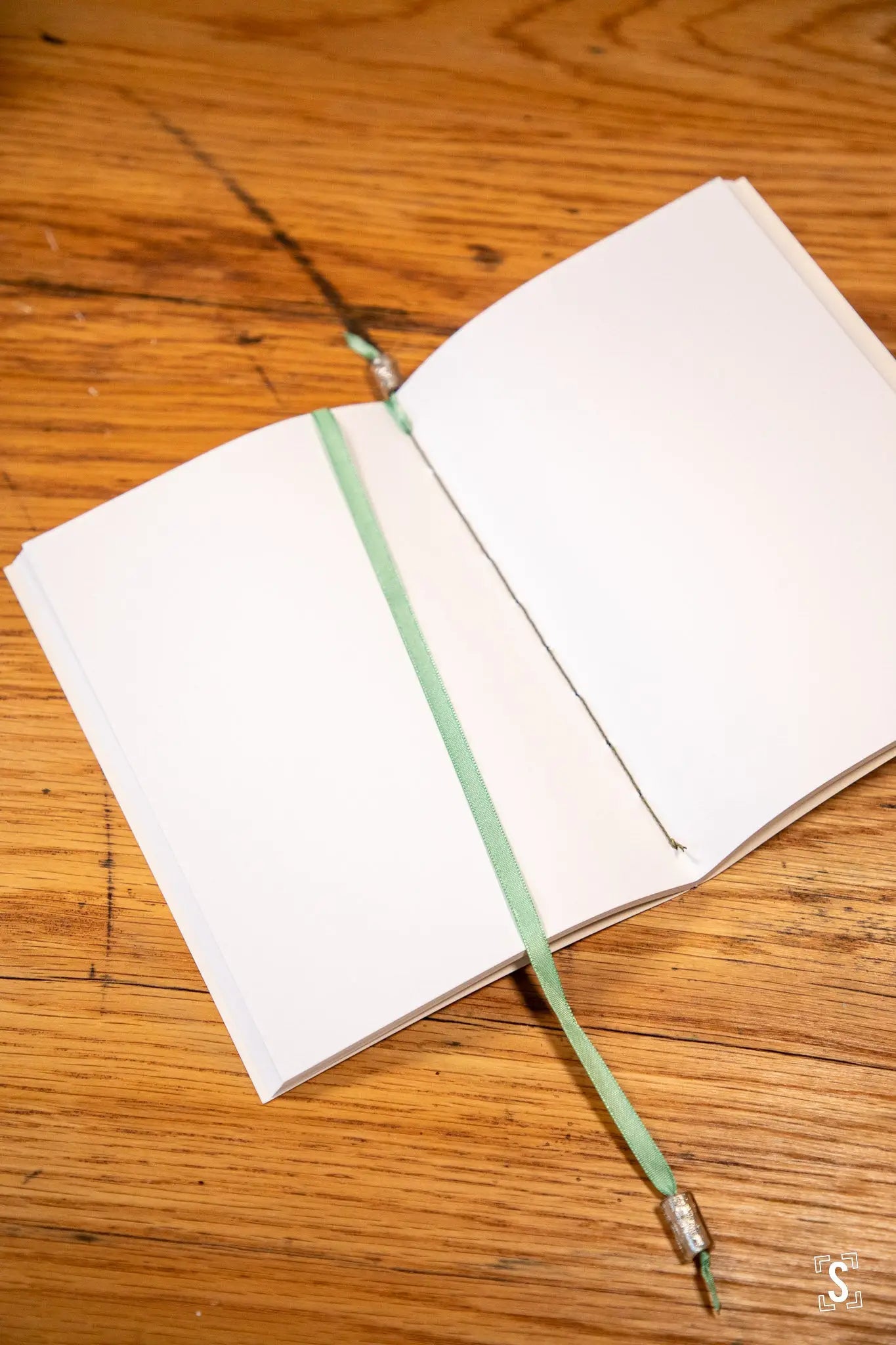 Open notebook with green bookmark showcasing handmade books, artfully designed and bound