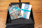 Gift box with two artfully wrapped presents featuring blue ribbons and decorative prints