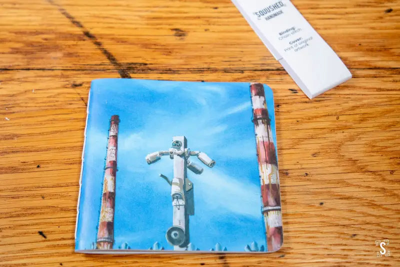 CD or DVD case artwork of a crucified robot against a blue sky for a Handmade Notebook with chain stitch binding