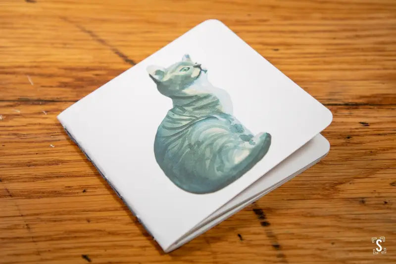 White napkin with blue-green watercolor cat illustration on Handmade Notebook with chain stitch binding