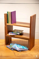 Wooden bookshelf with three shelves displaying various books and a handmade pocket notebook