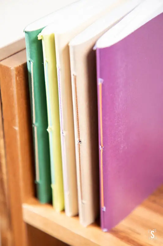 Row of colorful books on a shelf near a Handmade Pocket Notebook for stylish organization