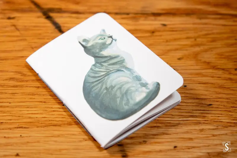 Pale blue-green ceramic hippo on white cover of a Handmade Pocket Notebook