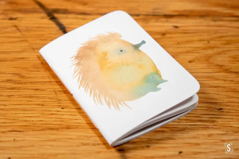 White handmade pocket notebook featuring a watercolor hedgehog design on the cover