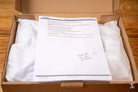 Open cardboard box with tissue paper and a document for Bookbinding Tools Kit contents