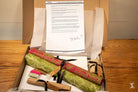 Open box with rolled fabric, scissors, and document for Coptic Stitch bookbinding materials