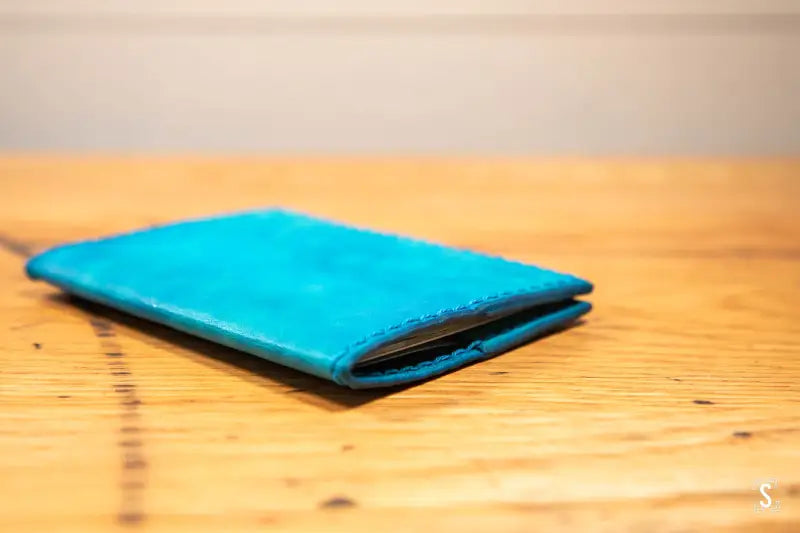 Bright blue leather passport holder case on a wooden surface at Leathercraft Workshop