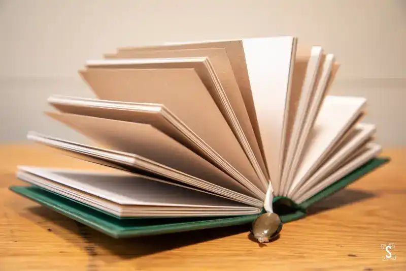 Open handmade book with fanned-out pages and green cover on wooden surface